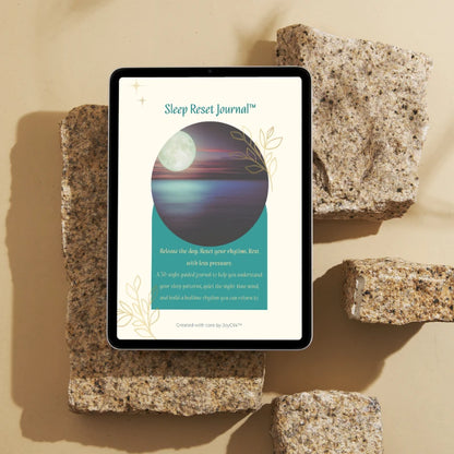 Sleep Reset Journal™ cover displayed on a tablet resting on textured stone blocks against a sand-coloured background.