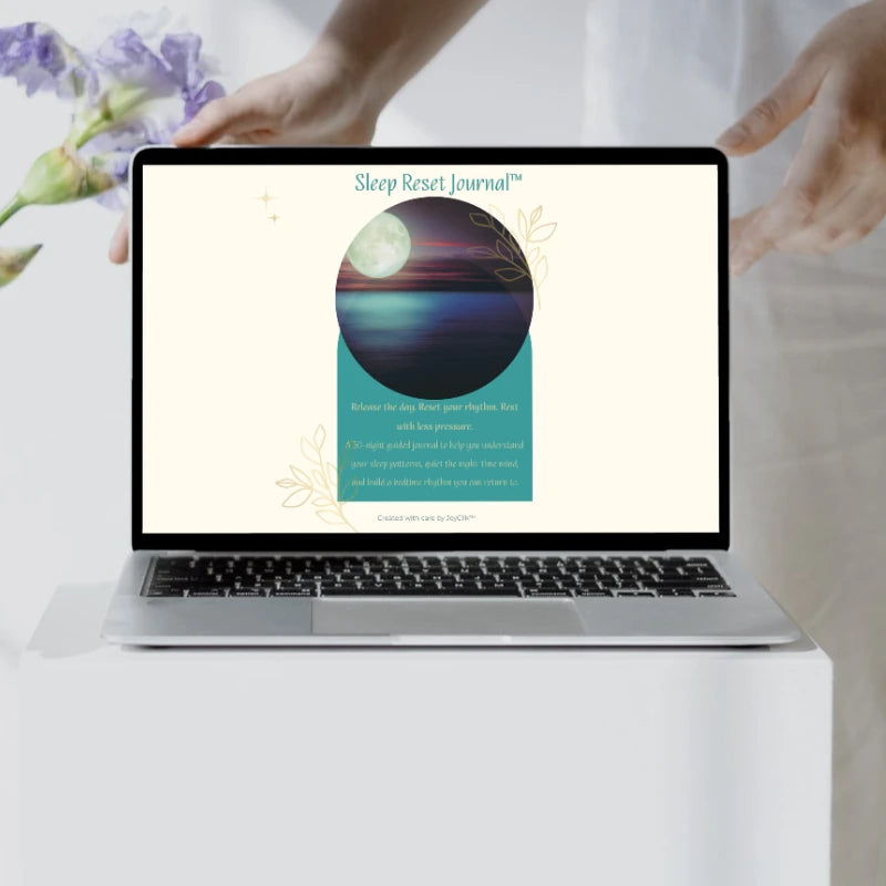 Sleep Reset Journal™ cover displayed on a laptop on a white table beside purple flowers.